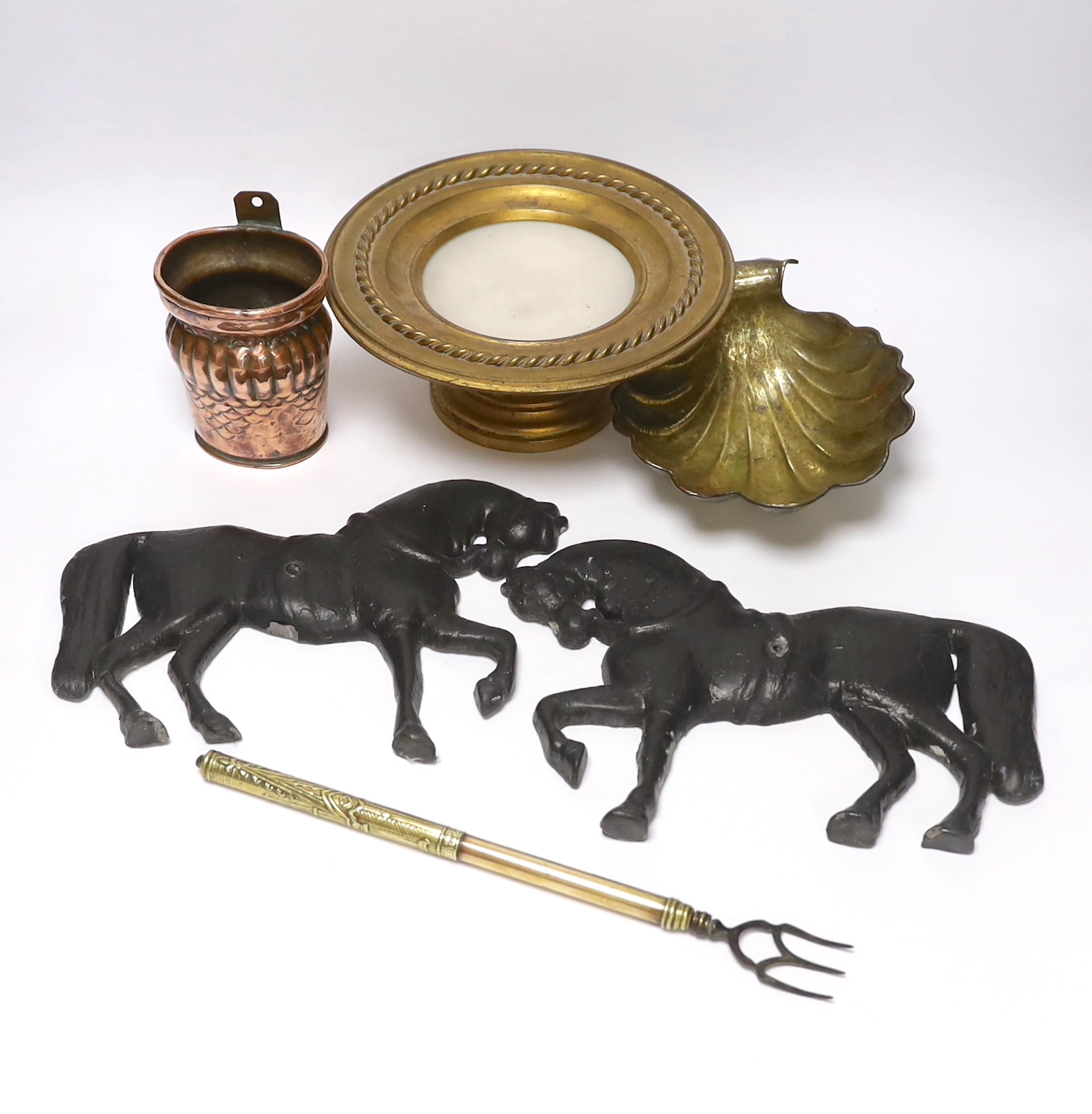 A group of metalware to include a pair of lead ‘horse’ wall mounts, a copper wall pocket, a, brass ‘scallop shell’ dish, a telescopic three pronged fork and an alabaster pedestal dish